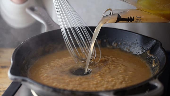 Pouring pan juices into browned roux while whisking.