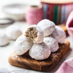 Mexican wedding cookies piled on a wooden board with Christmas ribbon in the background.