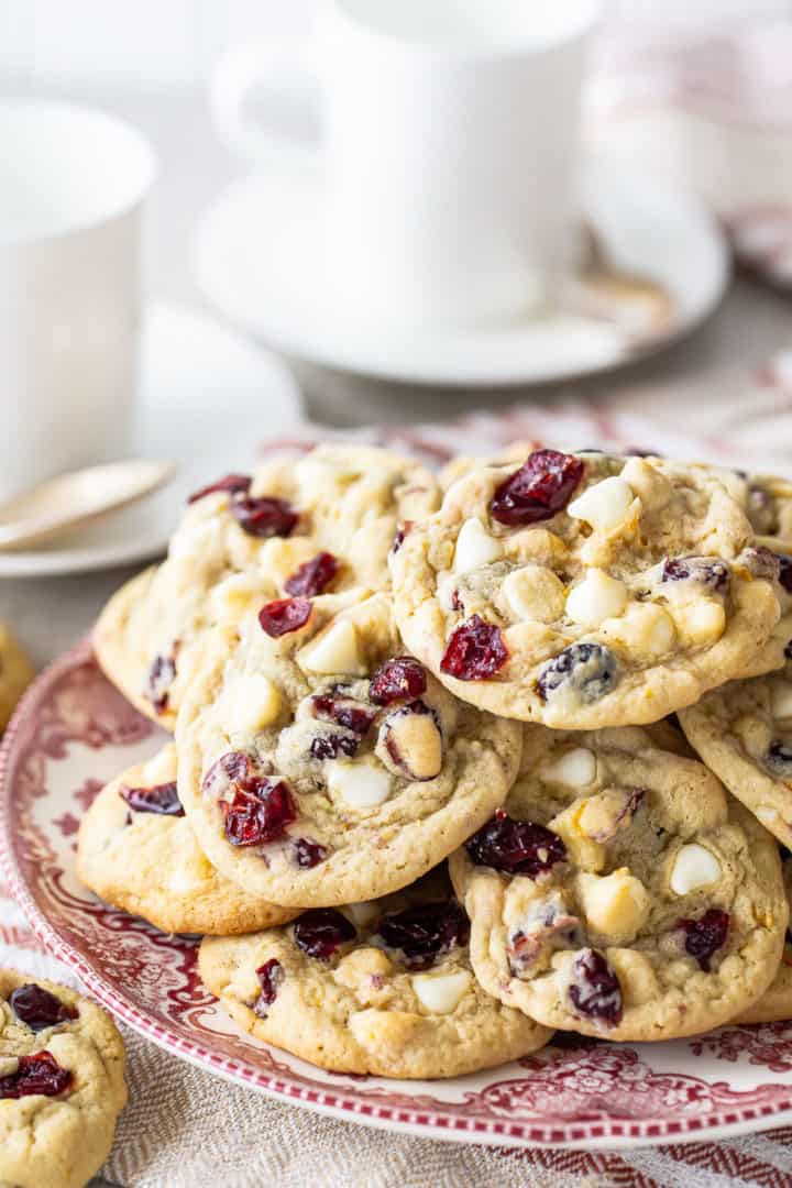 Close-up image of cranberry cookies arranged on a vintage plate with coffee cups in the background.