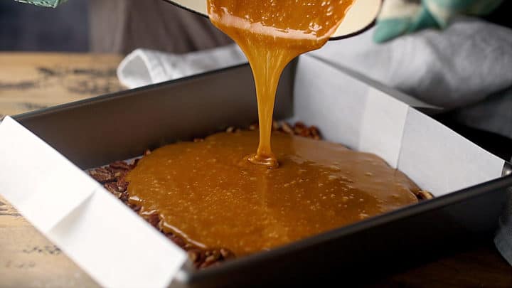 Pouring hot toffee mixture over toasted nuts.