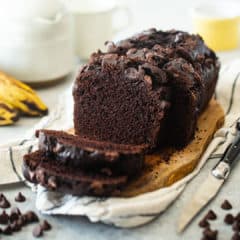 Chocolate banana bread presented on a wooden board with bananas in the background.