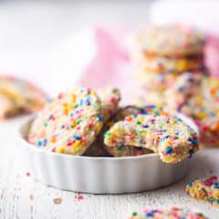 Funfetti cookies piled into a small white ceramic dish, with more cookies stacked in the background.