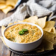 Jalapeno popper dip served in a white ceramic bowl with two slices of fresh jalapeno pepper on top.