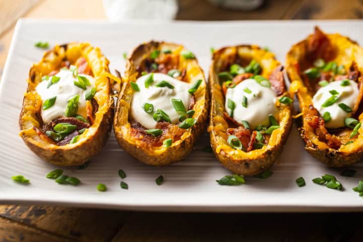Best potato skins recipe stuffed with cheddar cheese, crumbled bacon, sour cream, and scallions, served on a platter.