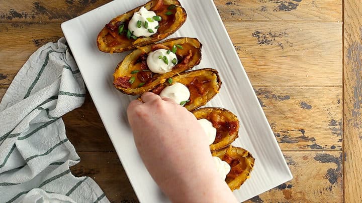 Topping potato skins with bacon, sour cream, and green onions.