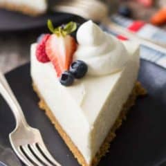 slice of cheesecake on black plate topped with strawberries, and whipped cream