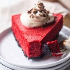 red velvet cheesecake topped with whipped cream on white plate