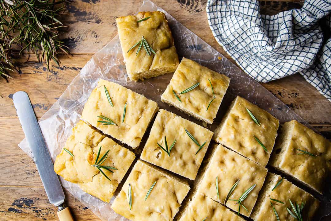 Overhead image of focaccia bread recipe, prepared and garnished with sea salt and fresh herbs.