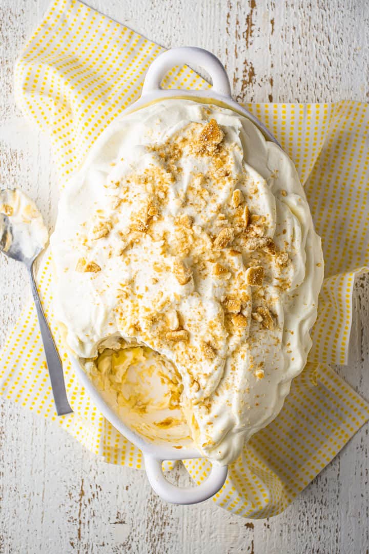 Overhead image of how to make banana pudding with layers of vanilla wafers, homemade vanilla pudding, sliced banana, and whipped cream.
