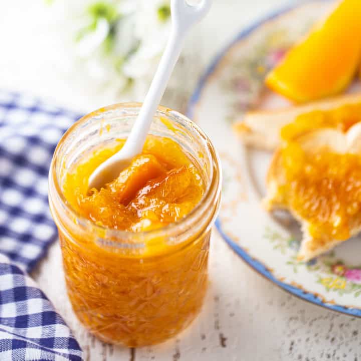 Marmalade in a glass jelly jar with a white ceramic spoon.