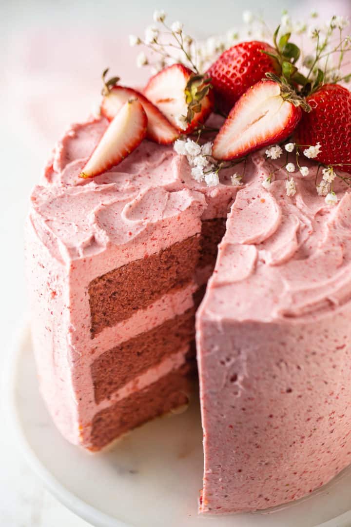 Close up image of the best strawberry cake recipe, garnished with fresh strawberries and fresh flowers.