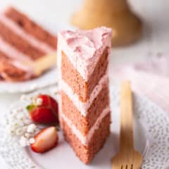 A slice of strawberry cake on a lacy white plate with a wooden fork.