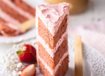 A slice of strawberry cake on a lacy white plate with a wooden fork.