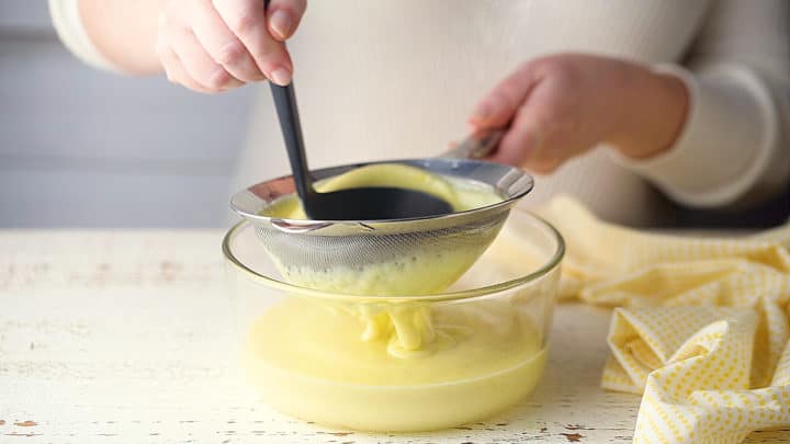 Passing homemade pudding through a sieve to remove any lumps.