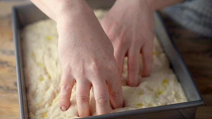 Pushing fingertips into focaccia dough to create dimples.