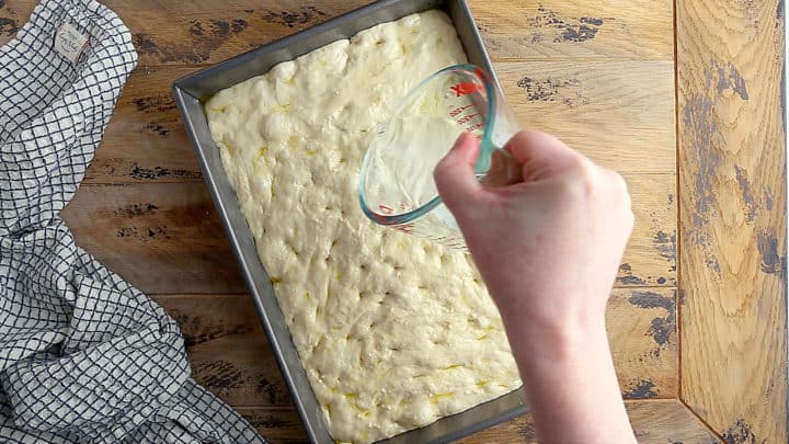 Pouring brine over unbaked focaccia.