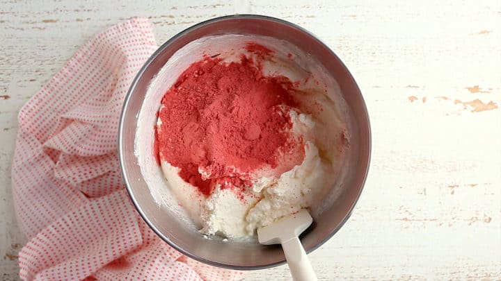 Adding strawberry powder to prepared buttercream frosting.