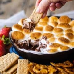 Hand dipping graham cracker into s'mores dip.