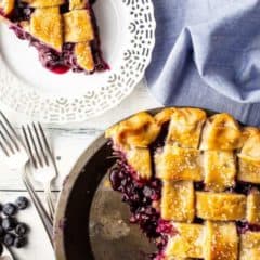 Berry pie slice on white plate, blueberry pie in pan.