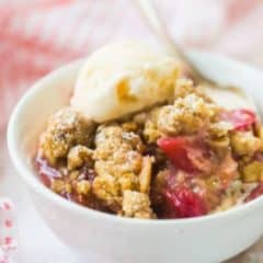 Rhubarb crisp in white bowl topped with a scoop vanilla ice cream.