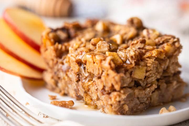 Close up image of a square of easy baked oatmeal, served with sliced apples, honey, and walnuts.