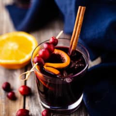 A glass of mulled wine, garnished with a cinnamon stick and fresh cranberries.