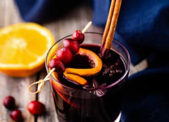 A glass of mulled wine, garnished with a cinnamon stick and fresh cranberries.