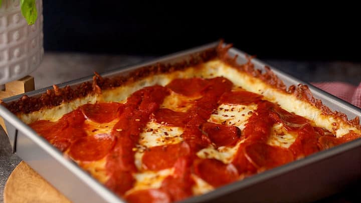 Detroit-style pizza baked in a square cake pan.