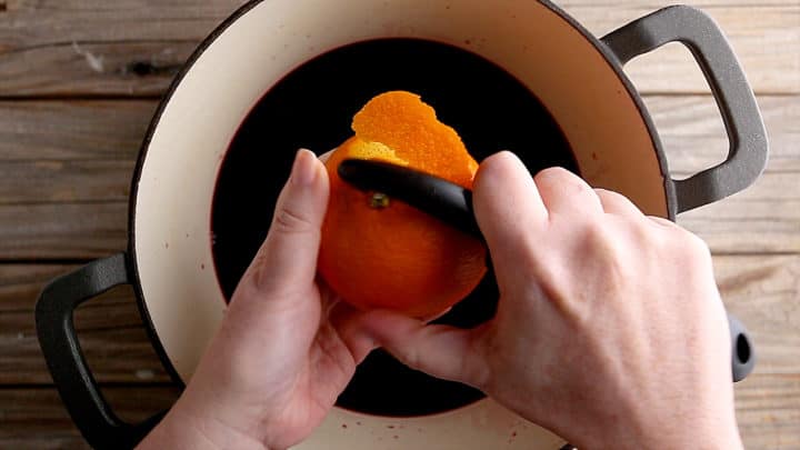 Removing the zest from an orange with a veggie peeler.