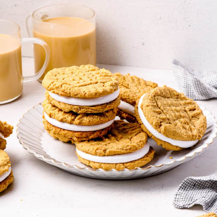 Fluffernutter cookies stacked on a white plate with cups of coffee in the background.