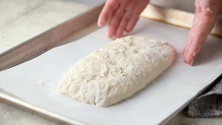 Shaping ciabatta loaf on a parchment-lined baking sheet.