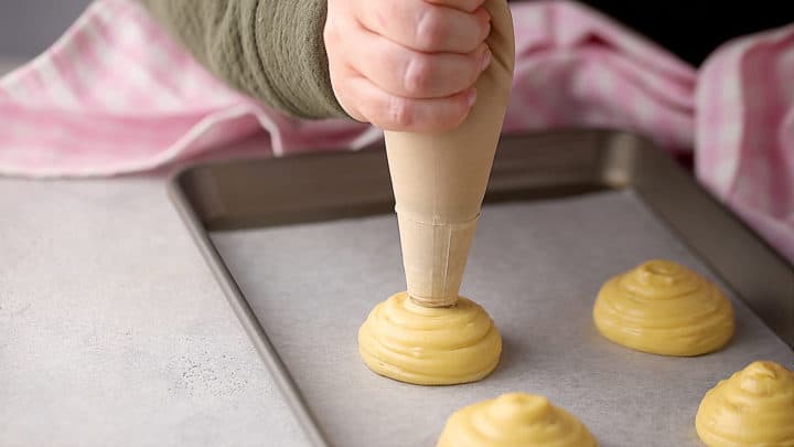 Piping pate a choux with a pastry bag.
