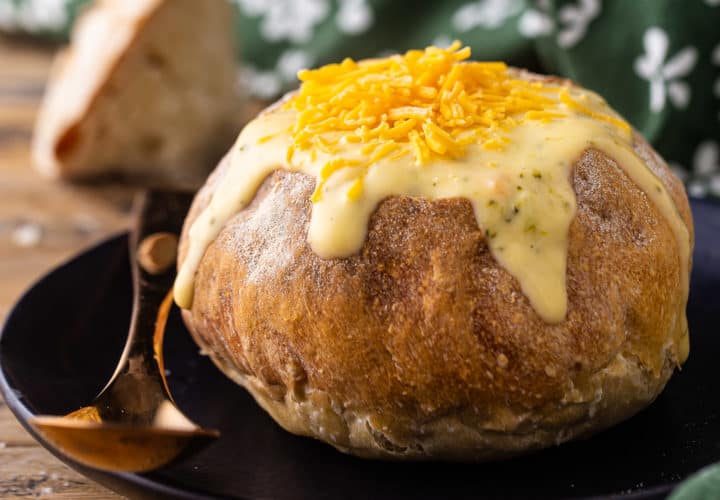 Bread bowl filled with soup on a dark plate with a copper spoon.