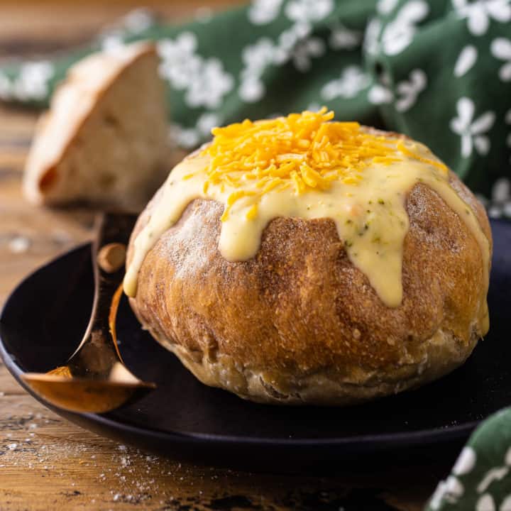 Bread bowl filled with soup on a dark plate with a copper spoon.
