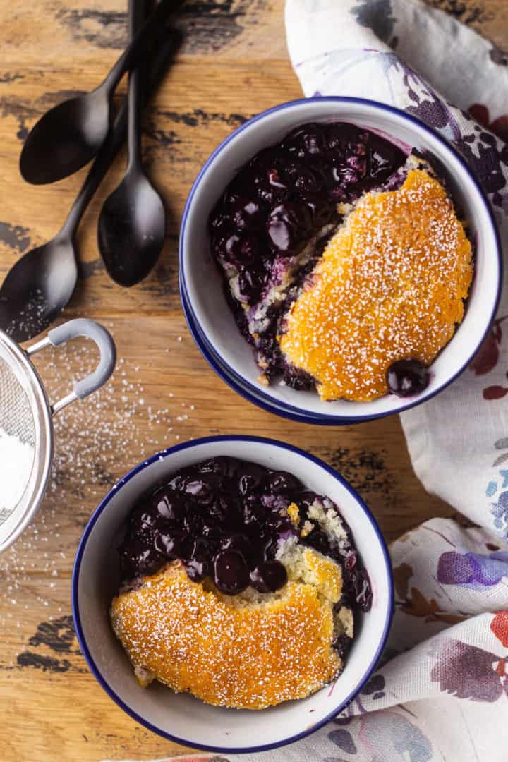 Overhead image of two bowls of easy blueberry cobbler on a wooden table with black spoons.