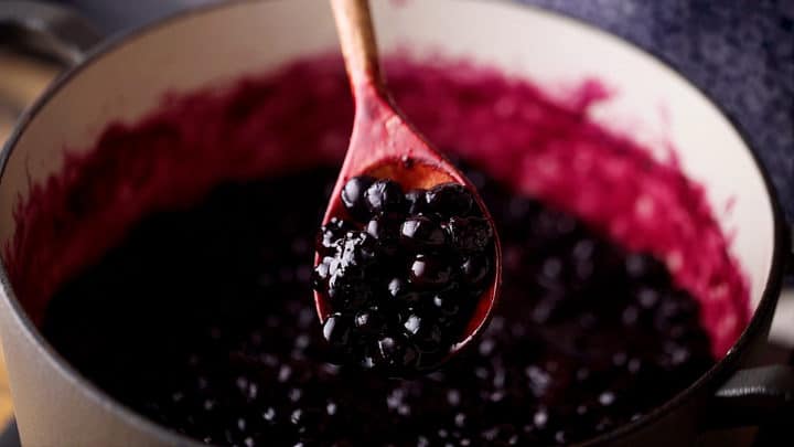 Cooked blueberry filling being spooned from a pot.