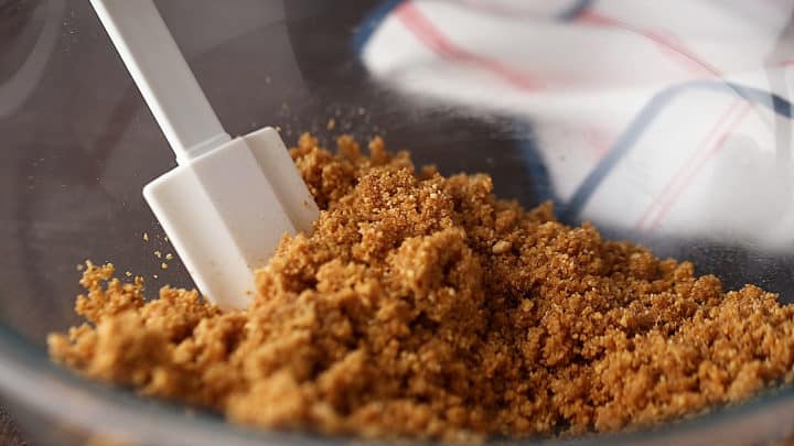 Graham cracker crust mixture in a glass bowl with a silicone spatula.