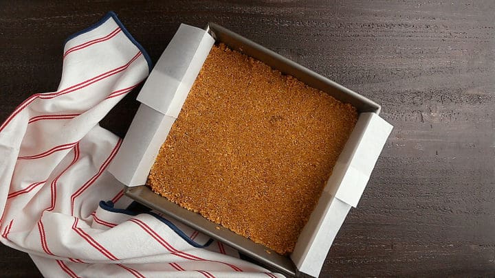 Graham cracker crust pressed into an even layer in a square pan.