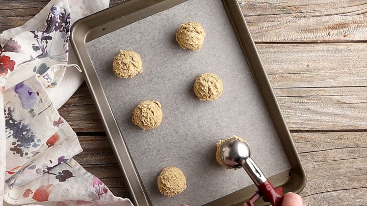Scooping brown sugar cookie dough onto a parchment-lined baking sheet.