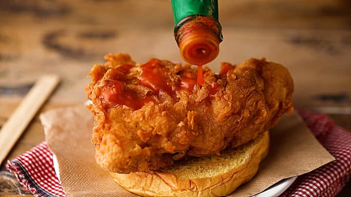 Topping fried chicken sandwich with hot sauce.
