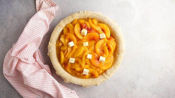 Unbaked peach pie dotted with butter.