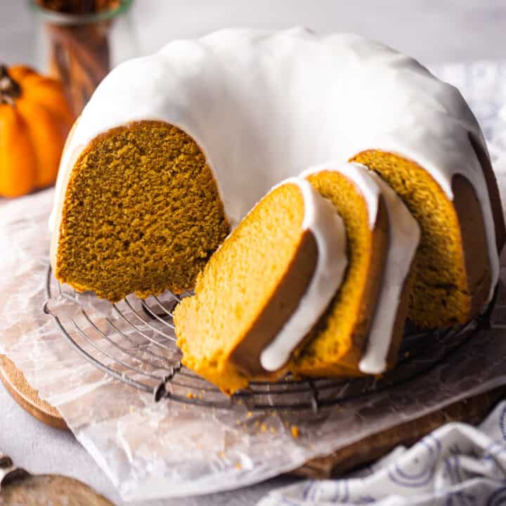 Pumpkin bundt cake with cream cheese glaze sliced and presented on a wire rack.