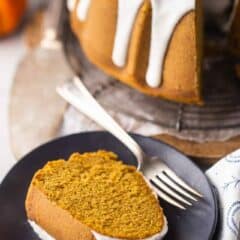 Slice of pumpkin spice bundt cake served on a dark blue plate, with the whole cake in the background.
