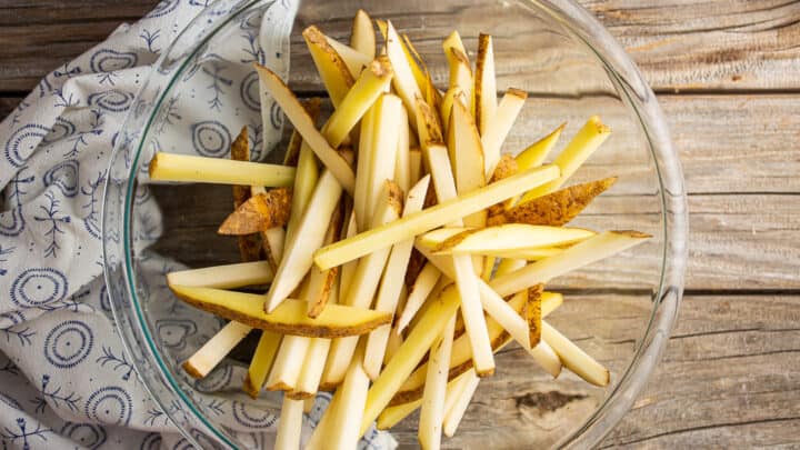Uncooked French fries in a large glass bowl.