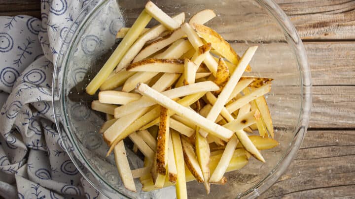 Tossing uncooked fries with oil, cornstarch, and salt.