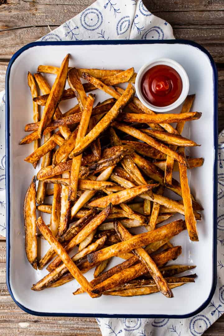 Baked French fries on an enameled tray with a blue and white cloth.