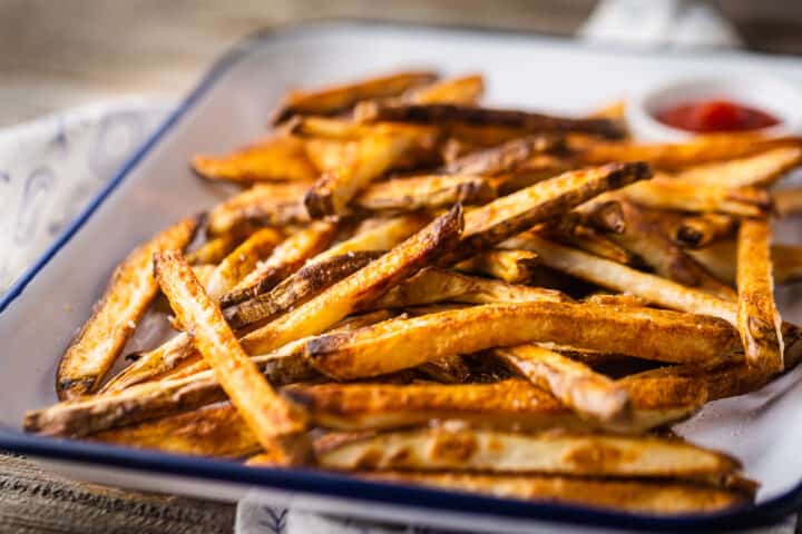 Tray of golden brown crispy oven fries, on a distressed wooden tabletop.