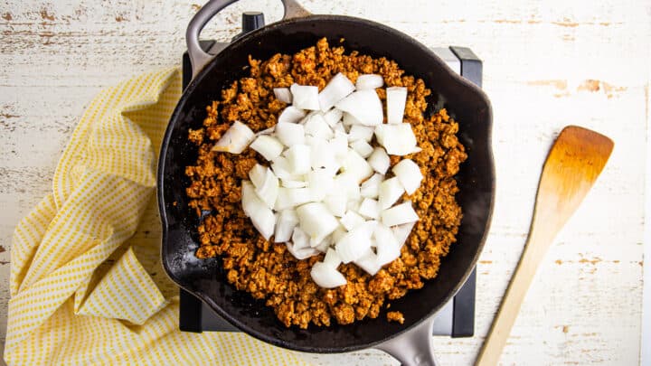 Cooking chorizo in a skillet with chopped onions.