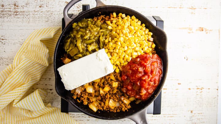 Making corn dip in a skillet with chorizo, onions, salsa, and diced green chiles.