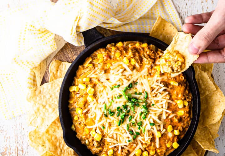 Scooping corn dip from a hot skillet with a corn chip.